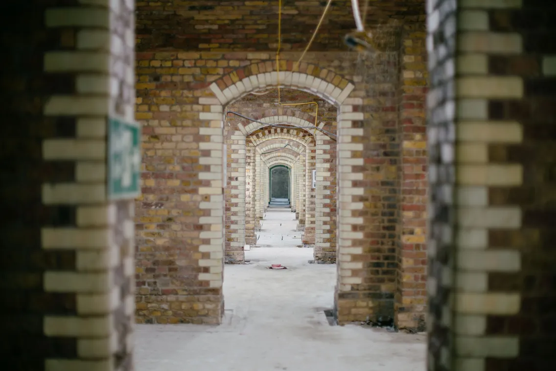 A brick-walled underground structure with arched doorways and covered equipment. Construction materials and protective coverings are visible.
